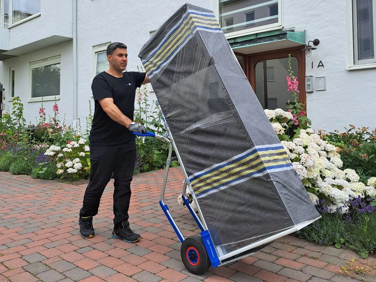 Medarbetare från Lyx Flytt transporterar en skyddsinpackad möbel på en transportkärra.